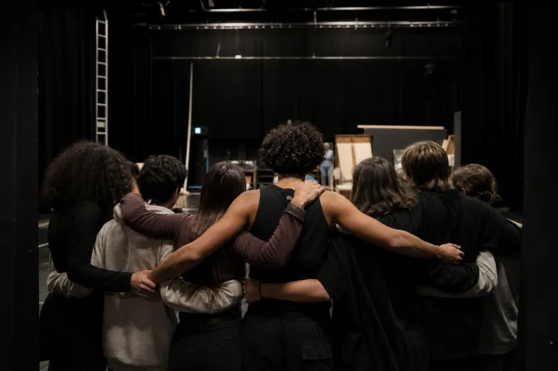 Photo d'un groupe de jeunes bras dessus bras dessous dans une salle de spectacle. 