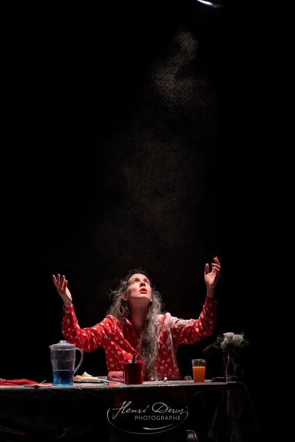 Photo d'une comédienne levant les bras au ciel, devant une table