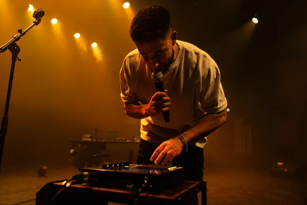 Photo d'un homme penché sur un table de mixage, avec un micro à la main